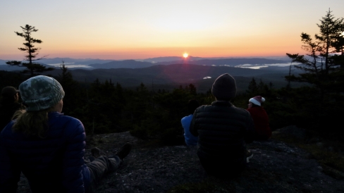 Dartmouth students sit on a mountainside watching the warm palette of sunrise colors as the sun breaches the horizon.