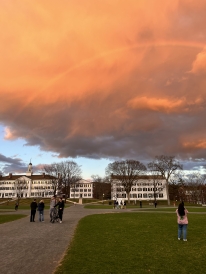 A photo of Dartmouth Hall. The sky is a vibrant orange, and a faint rainbow is visible.