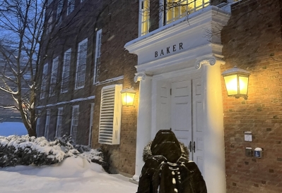 An image of a student walking through snowfall to Baker Library