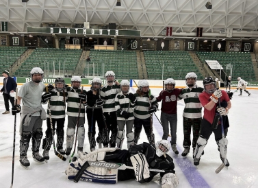 a group of Dartmouth students in hockey skates and helmets, mostly wearing green-and-white striped shirts
