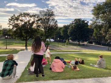 Group of students sitting on the lawn looking at the sunset from Dartmouth Hall