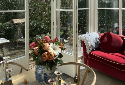 An image of a sunroom with a flowers on the table and a red couch in the corner.