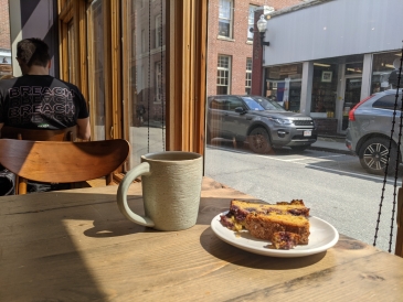 Picture of my cup of coffee and blueberry cornbread looking out the window of Still North Books & Bar