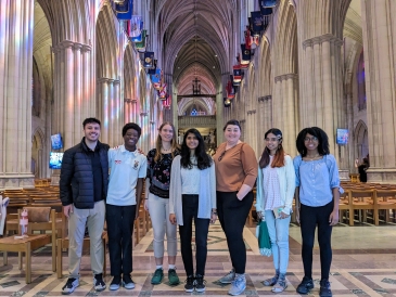 At the National Cathedral in the main hall with colored natural light from all of the stained glass windows and all of the state flags line the hall.
