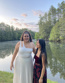 Posed picture of two friends in front of a pond and pink/purple sky