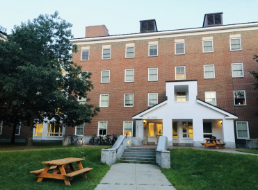 A ground view of Bilder Hall, a brick dorm building with white accents surrounded by grass and trees. 