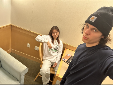 A selfie that my friend took featuring me sitting at a desk with a laptop open, and him striking a cool pose. 