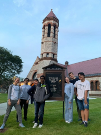 Interfaith LLC '27 at Rollins Chapel. Everyone is smiling and standing around the Rollins sign out front of the building.