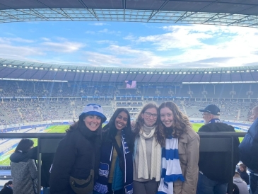 An image of four students standing in front of an enormous football stadium