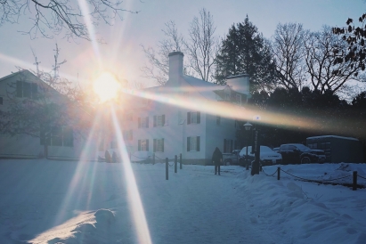 The sun rising in the background with a snowy path a white building in the foreground