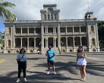 Image of Gabriel Gilbert, Sheen Kim, and Aaní Perkins in front of ʻIolani Palace.