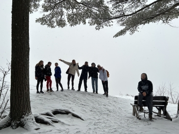 A group of 8 students huddle together at the top of Wright's Mountain. Although there isn't much of a sunset, the white fog looks beautiful!