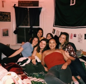 Abbi and her water polo team mates sitting on a dorm room bed and smiling during a team social