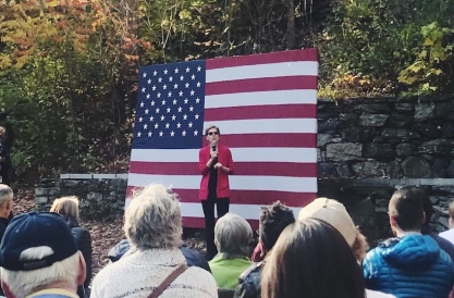 Sen. Warren speaking to a crowd outdoors, with an American flag in the background
