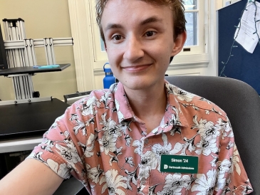 A smiling student in a pink floral shirt and a name tag that says "Simon '24, Dartmouth Admissions"