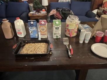 One large chocolate chip cookie in a baking pan and a variety of milks laid out on a table