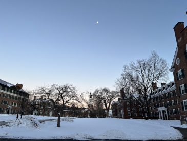 A photo of Baker Tower and the surrounding dorm buildings from Tuck Drive. The sun is setting, and there is snow on the ground.