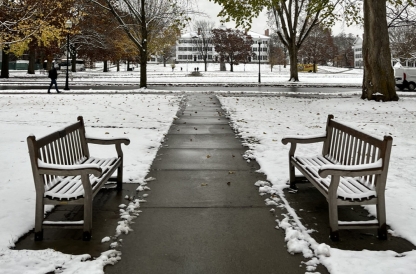 Two benches covered in a light layer of snow on either side of a concrete path