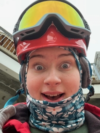 A selfie of me wearing my ski gear. My helmet is a pink-ish red, my goggles are blue, and my balaclava is teal with flowers on it.