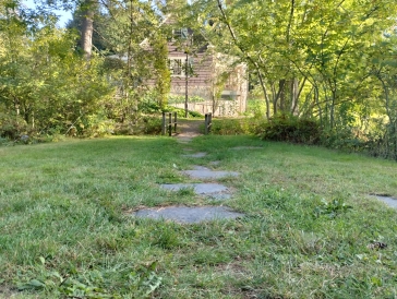 A picture of the Dartmouth outing club lodge at Occom Pond from the path off to the side of the building near the pond. The view of the lodge is partially obscured by trees. 