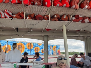 An image of a large painted mural on grain silos, from a boat where people are enjoying dinner.