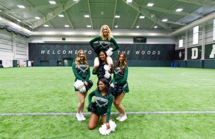 A group of cheerleaders in a dynamic formation, smiling and showcasing their team spirit during a media day.