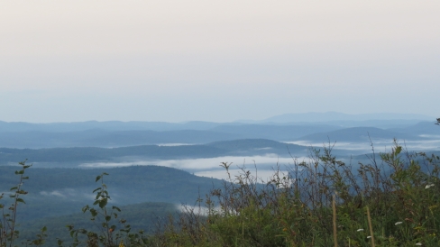 A landscape view of New Hampshire mountains carpeted in forests with misty clouds in the valleys.