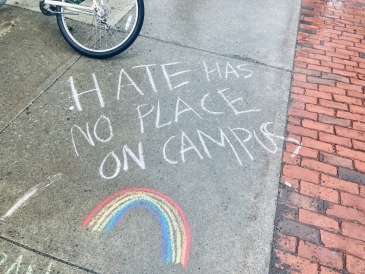 Chalk art that says "Hate has no place on campus" written in white, with a rainbow drawn underneath the words.