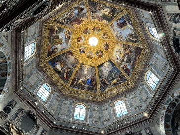 An upward shot of an intricately painted basilica ceiling. The ceiling is octagonal and decorated with religious imagery. 