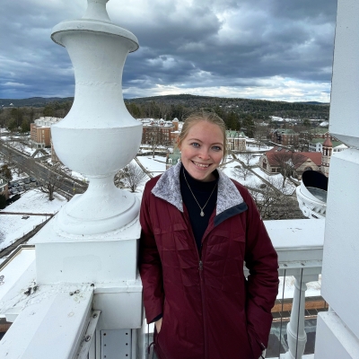 A girl wearing a red jacket with blonde hair on top of the bell tower of Baker-Berry Library