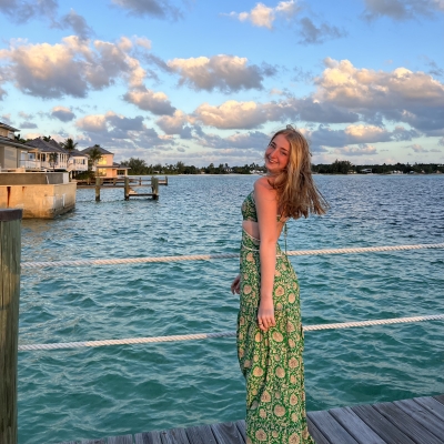Lauren in front of blue water wearing green dress, smiling