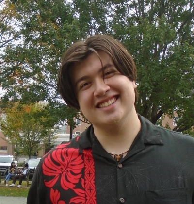 Image of Gabriel Gilbert '23; he is wearing a black aloha shirt with a red leaf pattern that runs from his shoulder down the left half of his shirt.