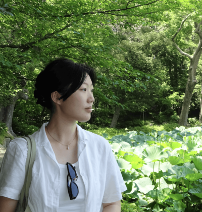 Youmi looking to the side in front of greenery