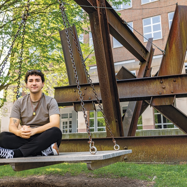 A photo of Batuhan Sarideded '26 sitting on X-Delta, a public sculpture outside Baker-Berry Library