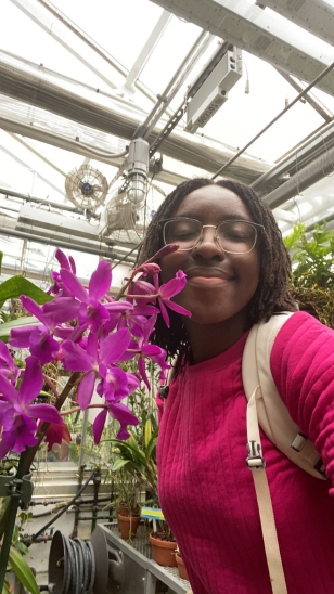 A picture of me in the Dartmouth Greenhouse next to a magenta orchid.