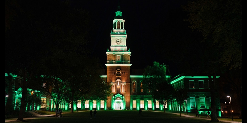 A photo of Baker Library lit up with green lights for the 250th