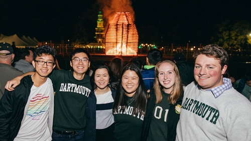 A photo of six Dartmouth alumni standing together in front of the Dartmouth Homecoming bonfire