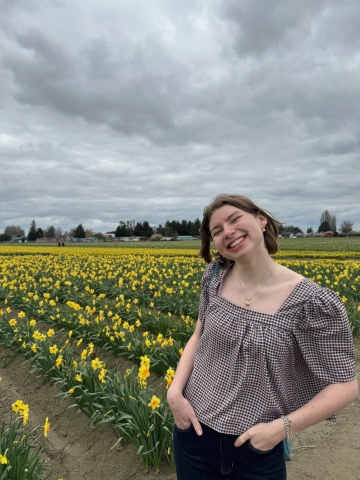 Julia standing in a field of daffodils in a pair of jeans and a striped red top.