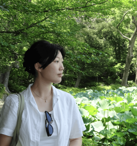 Youmi looking to the side in front of greenery