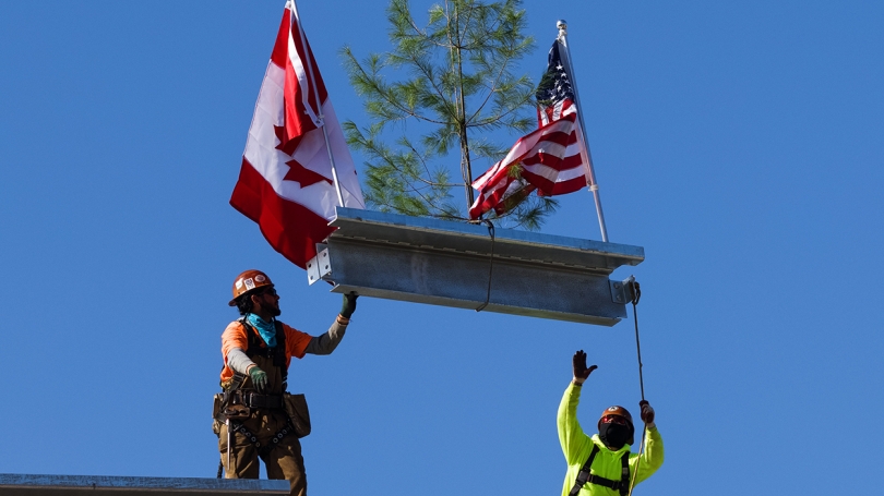 Culminating the topping-off ceremony, workers lower the beam into place.