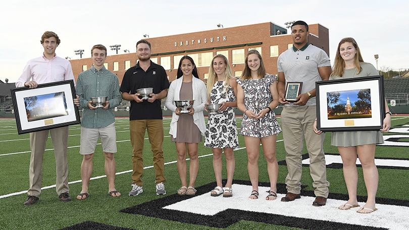 a group of students standing in a line on a football field holding awards