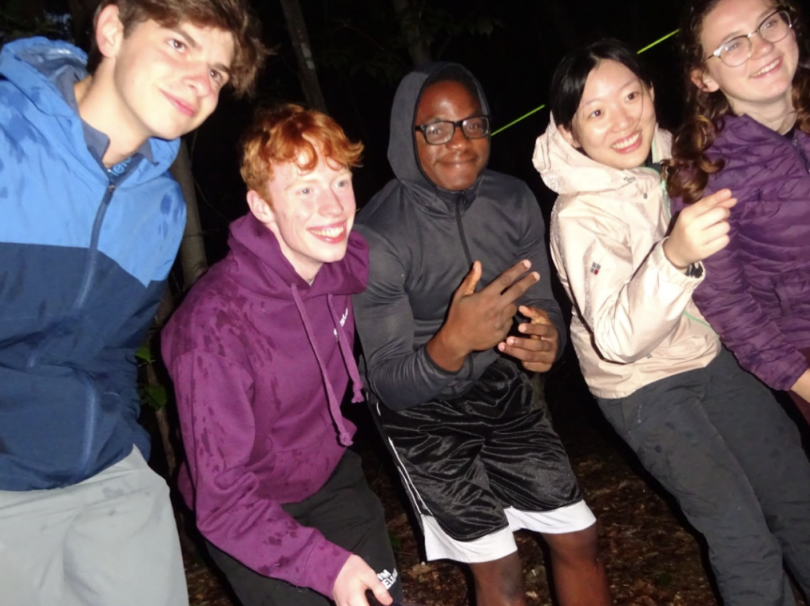five first-year students standing side-by-side pointing to something in the distance and smiling.