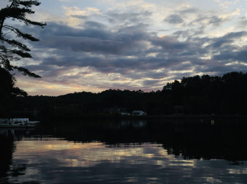 In the sky, the clouds are dyed with colors of the sunset. The sky and mountains in the distance reflect on the clear river.