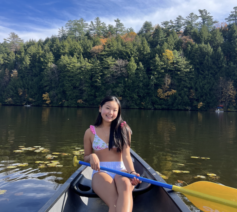 Madison sitting on a canoe and holding a yellow canoe paddle on a sunny fall day