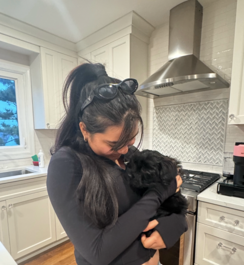 A girl in a black outfit cuddling a tiny black puppy in a bright, modern kitchen