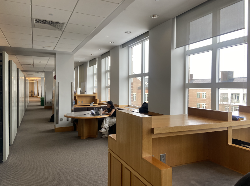 Wooden study desks line the left wall. They sit underneath huge windows with sunlight shining through.