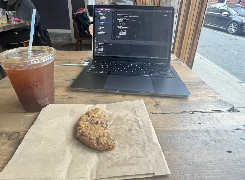 Picture of a desk at Still North, with a laptop with a cup of iced coffee and a cookie