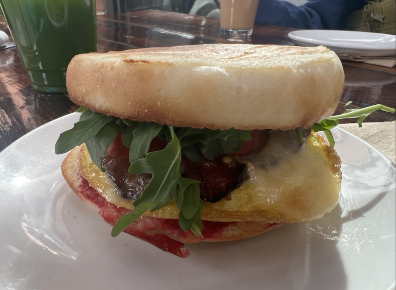 Picture of a breakfast sandwich with eggs, bacon, red beets, tomatoes, and kale