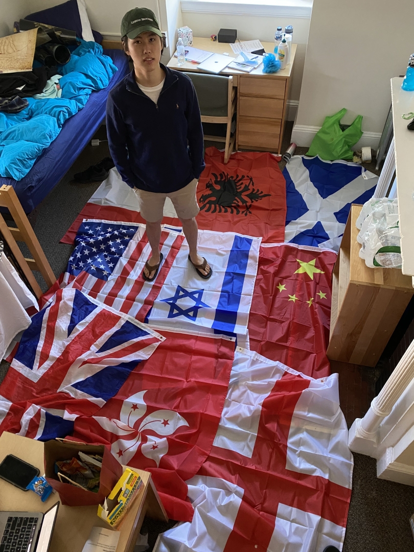 Nick, an international student from the U.K. and Hong Kong, stands on top of a bunch of flags in his dorm room.