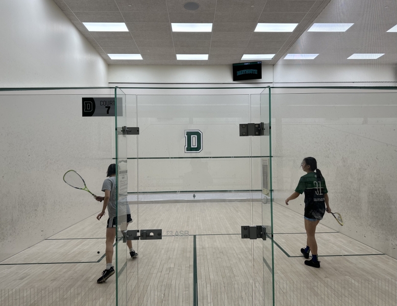 An action shot of two girls playing squash from outside the court